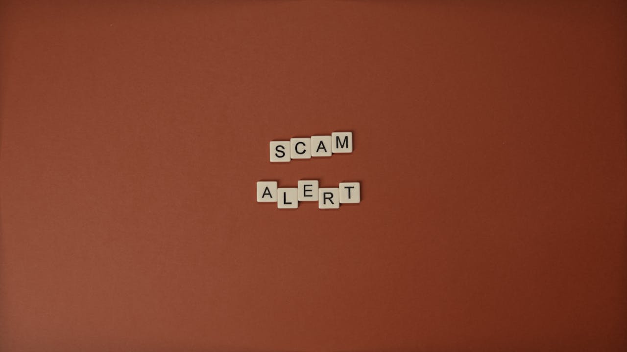 Scrabble tiles spelling Scam Alert on a brown surface indicating caution.